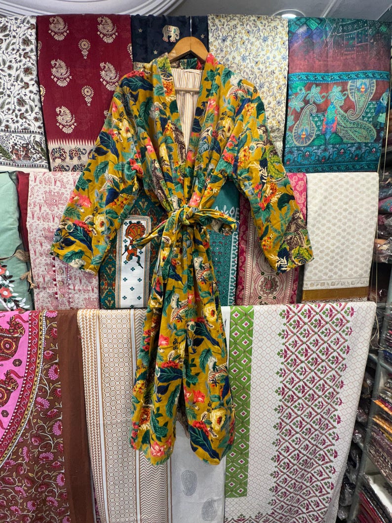May include: A mustard yellow kimono robe with a floral and animal print. The robe has a tie belt and long sleeves.