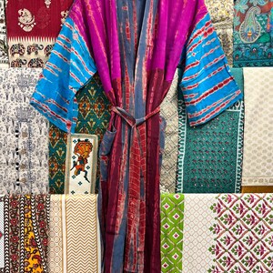 May include: A long, purple, blue, and red tie-dye robe with a sash. The robe is made of a soft, silky fabric and has a relaxed fit. The robe is hanging on a wooden hanger in front of a wall of colorful fabric.