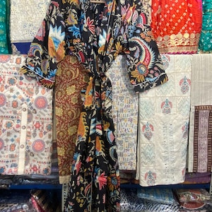 May include: A black kimono-style robe with a vibrant floral pattern in shades of blue, red, yellow, and orange. The robe has a white trim and a matching tie. The robe is hanging on a wooden hanger.