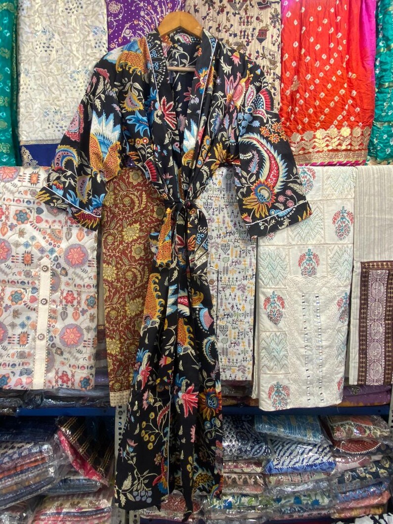 May include: A black kimono-style robe with a vibrant floral pattern in shades of blue, red, yellow, and orange. The robe has a white trim and a matching tie. The robe is hanging on a wooden hanger.
