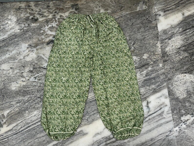 May include: Green patterned trousers with a drawstring waist. The trousers feature a repeating floral design in shades of green and white. The trousers have a relaxed fit and are made of a lightweight fabric.