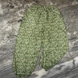 May include: Green patterned trousers with a drawstring waist. The trousers feature a repeating floral design in shades of green and white. They have a relaxed fit and are made of a lightweight fabric.
