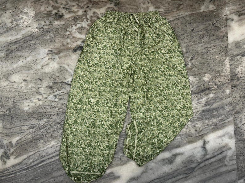 May include: Green patterned trousers with a drawstring waist. The trousers feature a repeating floral design in shades of green and white. They have a relaxed fit and are made of a lightweight fabric.