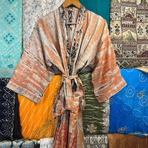 May include: A long-sleeved kimono robe featuring a tie-dye pattern in shades of peach, cream, and charcoal gray. The garment has a wide collar, an open front, and a matching fabric tie belt at the waist, displayed on a wooden hanger.