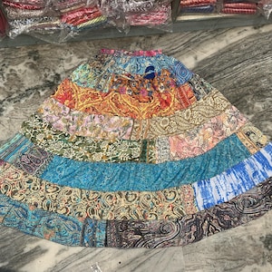 May include: A patchwork skirt in a range of colours including blue, orange, green, and pink. The skirt is made from various patterned fabrics, with a flowing shape. The design incorporates paisley, floral, and abstract patterns, and is constructed from multiple fabric panels.