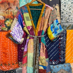 May include: A patchwork kimono robe with a variety of colorful fabric patterns. The robe has a gold trim and a matching belt. The background features various patterned fabrics.