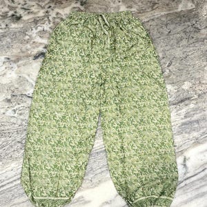May include: Green patterned trousers with a drawstring waist. The trousers feature a repeating floral design in shades of green and white. The fabric appears lightweight and suitable for casual wear.