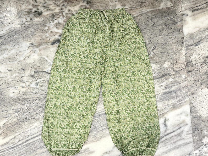 May include: Green patterned trousers with a drawstring waist. The trousers feature a repeating floral design in shades of green and white. The fabric appears lightweight and suitable for casual wear.