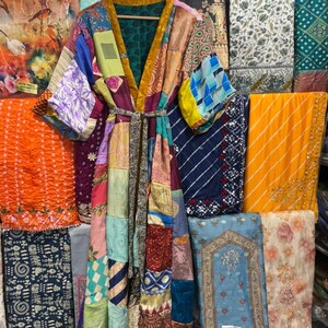 May include: A patchwork kimono robe with a variety of colorful fabric patterns, including floral, geometric, and abstract designs. The robe has a belt and is hanging on a wooden hanger. The background features various textiles.
