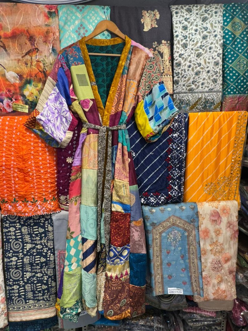 May include: A patchwork kimono robe with a variety of colorful fabric patterns, including floral, geometric, and abstract designs. The robe has a belt and is hanging on a wooden hanger. The background features various textiles.