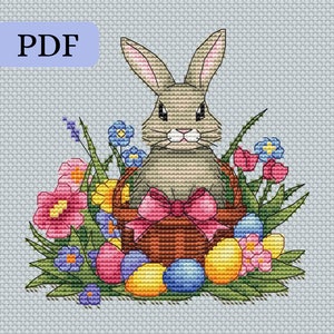 May include: Cross-stitch pattern featuring an Easter bunny in a basket surrounded by colorful eggs and flowers. The bunny has tan fur and a pink bow. The eggs are pink, yellow, and blue. The text "PDF" is in a light blue box in the upper left corner.