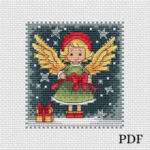 Puede incluir: Un patrón de punto de cruz que representa un ángel de Navidad con alas doradas, un lazo rojo y un vestido verde. El ángel sostiene una caja de regalo y está de pie sobre un fondo nevado con estrellas.