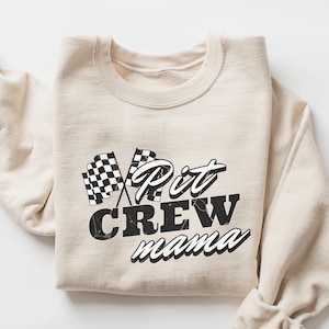 May include: Sand-colored sweatshirt with a black and white checkered flag graphic and the text "Pit Crew mama" in a vintage style font.