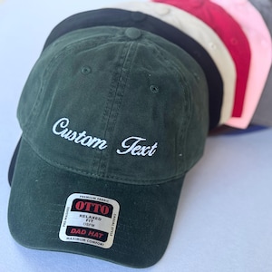 May include: A collection of pre-washed, relaxed-fit dad hats in various colors, including green, black, tan, red, pink, and gray. The green hat features the embroidered text "Custom Text" in white. The hats are made of premium fabric and are OSFM (One Size Fits Most).