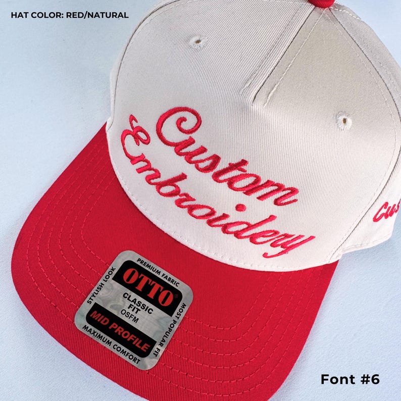 May include: A red and natural-colored baseball cap with the words "Custom Embroidery" embroidered in red script. The hat features a red brim and a "OTTO" brand sticker. The text "Font #6" is also visible.