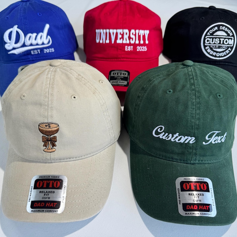 May include: A collection of baseball caps in various colors, including blue, red, black, tan, and green. Each cap features embroidered text or a design. The blue cap says "Dad", the red cap says "University", and the green cap says "Custom Text".