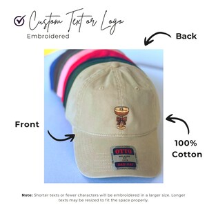 May include: A tan baseball cap with an embroidered cocktail design. The cap is made of 100% cotton and features the text "Custom Text or Logo" and "Embroidered". The cap has a curved brim and an adjustable strap. The back of the cap is visible.