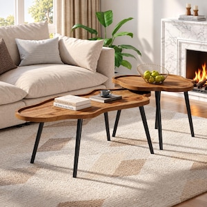 May include: A set of two nesting coffee tables with irregular, organic-shaped wooden tops and three slender black metal legs each. The tables feature a natural wood grain finish, providing a functional surface for books and a bowl of green apples.