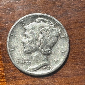 Può includere: Una moneta d'argento da dieci centesimi di tipo Mercury dime raffigurante il profilo della Libertà con un berretto alato, con il testo LIBERTY, IN GOD WE TRUST e l'anno 1943 chiaramente visibili sulla faccia della moneta circolare.