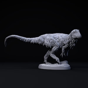 Puede incluir: Un modelo gris, detallado, impreso en 3D de un dinosaurio emplumado. El dinosaurio está en posición de carrera con la cola levantada y la cabeza girada hacia un lado. El modelo está colocado sobre una pequeña base redonda.