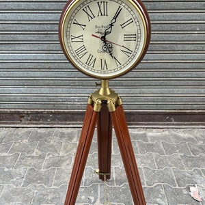 May include: A vintage-style clock with Roman numerals on a wooden tripod stand. The clock face is cream-colored with gold accents and features the text "Das Smith Est. 1770 London".
