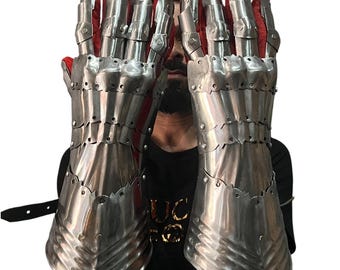 May include: A pair of polished steel gauntlets with articulated fingers and red interior lining. The medieval-style armor gloves are designed to protect the hands and wrists. Rivets secure the metal plates, and a leather strap is visible.