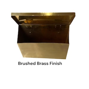 May include: A rectangular wall-mounted mailbox or storage bin made of metal with a brushed brass finish. The container features a hinged lid at the top and an open interior compartment. The text "Brushed Brass Finish" is printed below.