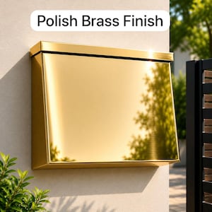May include: A rectangular wall-mounted mailbox with a highly reflective, polished brass finish. The mailbox features a flat top lid and a smooth, angled front panel. A white label above the mailbox displays the text Polish Brass Finish.