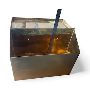 May include: A rectangular brass wall-mounted bin with an open top and a hinged lid. A metal ruler is placed inside, showing a height measurement of approximately 12 inches. The brass has a polished, reflective surface with visible mounting holes.