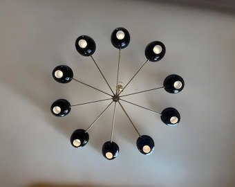 May include: A gold-toned ceiling light fixture with eight black globe-shaped shades. The shades have a white interior and are illuminated with light bulbs.