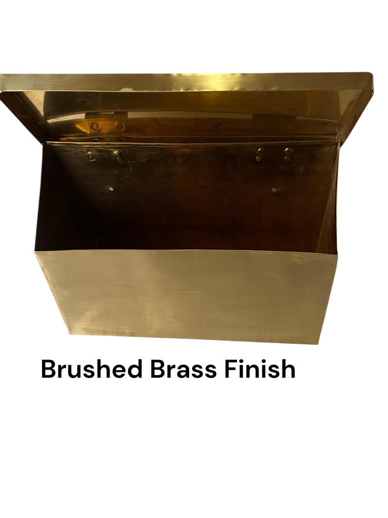 May include: A rectangular metal wall-mounted mailbox with a hinged lid and an open top section. The object features a metallic gold-toned surface with a brushed brass finish. The text "Brushed Brass Finish" is printed below the object.