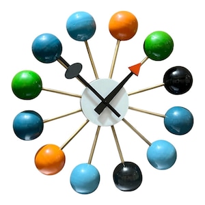 Peut inclure: Une horloge murale colorée de style moderne du milieu du siècle avec un cadran blanc et des aiguilles noires. L'horloge comporte 12 sphères de différentes couleurs, notamment bleu, vert, orange et noir, attachées au cadran.