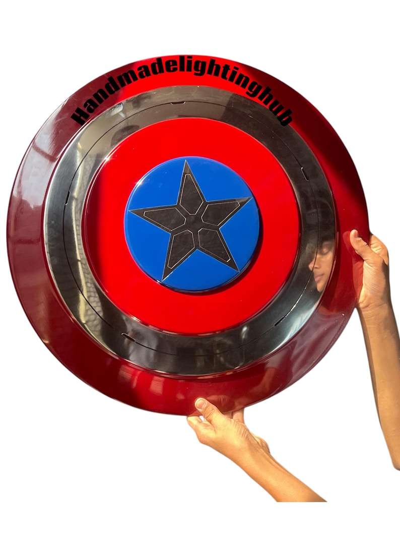 Puede incluir: Un escudo rojo, plateado y azul con un dise&ntilde;o de estrella. El escudo tiene forma circular, con un anillo exterior rojo, un anillo central plateado y un centro azul con una estrella negra. El texto "Handmadelightinghub" est&aacute; impreso en el anillo exterior.