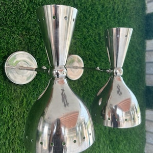 May include: A pair of silver wall sconces with a modern design. Each sconce has a round base and a cone-shaped shade with holes.