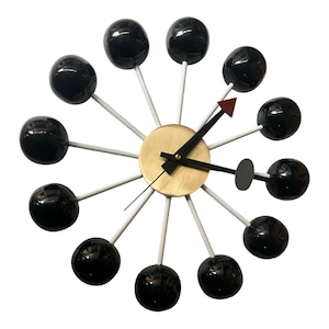 Może przedstawiać: Czarno-biały zegar z złotą tarczą i czarnymi wskazówkami. Zegar ma 12 czarnych kul wokół tarczy, każda połączona z środkiem białym prętem.