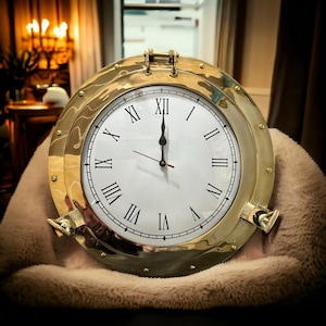 Può includere: Un orologio dorato con numeri romani e un quadrante bianco. L'orologio è impostato alle 12:00 e ha una cornice color ottone.