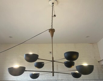 May include: A modern gold and black chandelier with six black bowl-shaped shades. The chandelier has a central stem with arms extending out to the shades.