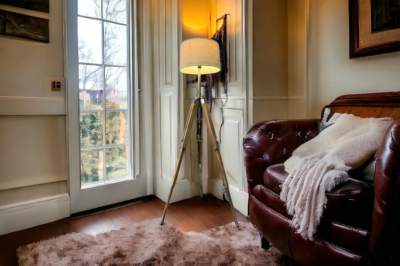 Puede incluir: Un sill&oacute;n de cuero marr&oacute;n con una manta blanca se encuentra en una habitaci&oacute;n con suelo de madera y una alfombra blanca. Una l&aacute;mpara de pie de tr&iacute;pode con una pantalla blanca est&aacute; en la esquina de la habitaci&oacute;n.