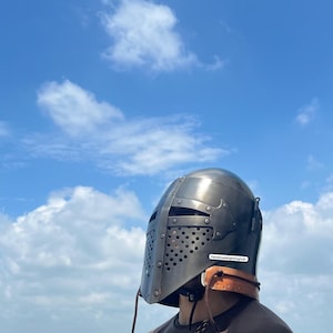 Pode incluir: Um capacete prateado com uma viseira e uma correia de couro. O capacete tem um design perfurado e o texto "Handmadelightinghub" &eacute; vis&iacute;vel na correia.