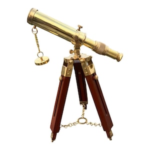 May include: A brass telescope with a wooden tripod. The telescope is gold in color and has a chain attached to it. The tripod is dark brown wood.