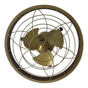 May include: A gold-toned ceiling fan featuring three blades and a protective cage. The fan is set within a dark brown wooden ring. The design has a vintage aesthetic, suitable for a classic interior.