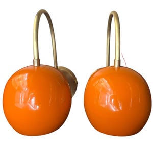 May include: A pair of orange globe wall lights with brass arms. The lights have a modern, mid-century design.