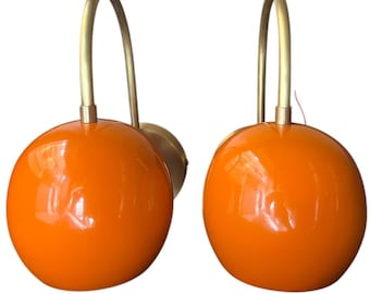 May include: A pair of orange globe wall sconces with brass arms. The sconces have a modern, mid-century design.