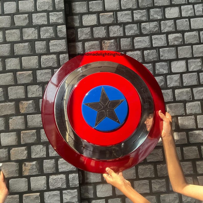 Puede incluir: Un escudo rojo, plateado y azul con un dise&ntilde;o de estrella. El escudo tiene un anillo exterior rojo, un anillo central plateado y un centro azul con una estrella negra. El escudo se sostiene contra una pared de ladrillos grises.