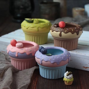 Op de afbeelding: Vier kleurrijke cupcake-vormige potten met verschillende toppings, waaronder avocado, chocolade, macarons en blauwe bessen. De potten zijn gemaakt van keramiek en hebben een geglazuurde afwerking.
