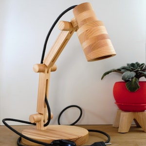 May include: A wooden desk lamp with a black cord and a wooden shade. The lamp is adjustable and has a simple design.
