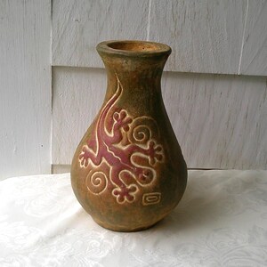May include: A handcrafted, brown ceramic vase with a lizard design in red and cream. The vase has a wide base, a narrow neck, and a textured surface. The lizard design is carved into the vase's surface.