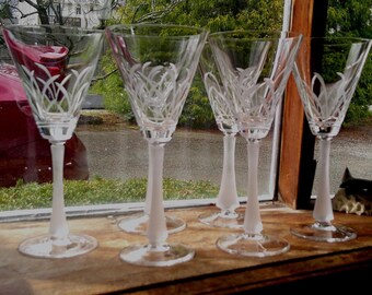 May include: Six clear glass wine glasses with frosted stems and etched designs. The glasses are arranged in a row on a wooden surface.