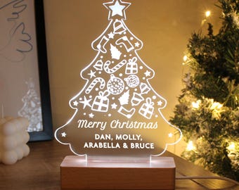 May include: A white acrylic Christmas tree light with a wooden base. The tree is decorated with white Christmas ornaments, stars, candy canes, and stockings. The light has a message that reads "Merry Christmas Dan, Molly, Arabella & Bruce".