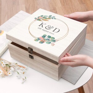 May include: A white wooden keepsake box with a gold-toned circle and floral design. The box has a hinged lid and two clasps. The text "K&D 6th August 2023" is printed on the lid.